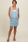 woman wearing a light denim maternity overall dress with pockets and a white tank top underneath