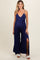 woman wearing a navy blue maternity jumpsuit with a plunging neckline, side slits, and a waist tie, showcasing her baby bump