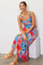 woman wearing a colorful patterned maxi dress with a square neckline and smiling while sitting on a white block