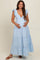 woman wearing a light blue tiered maternity dress with ruffled sleeves and cradling her baby bump