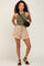 woman wearing olive green ribbed tank top and tan frayed hem drawstring shorts with black crossbody bag