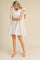 woman wearing a white short sleeve flounce dress with a ruffled neckline and a tiered skirt