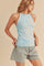 woman wearing a light blue ribbed tank top and denim shorts, posing with one hand on her hip
