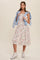 woman wearing a white floral midi dress with a tied blue shirt and white sneakers