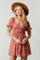 woman wearing a floral pink short dress with puff sleeves and a smocked waist, accessorized with a wide-brimmed hat