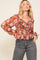 woman wearing a floral long sleeve blouse with a smocked bodice and ruffled cuffs paired with high-waisted jeans