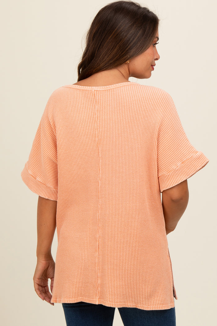 woman wearing a light orange short sleeve maternity top with a relaxed fit and side slits