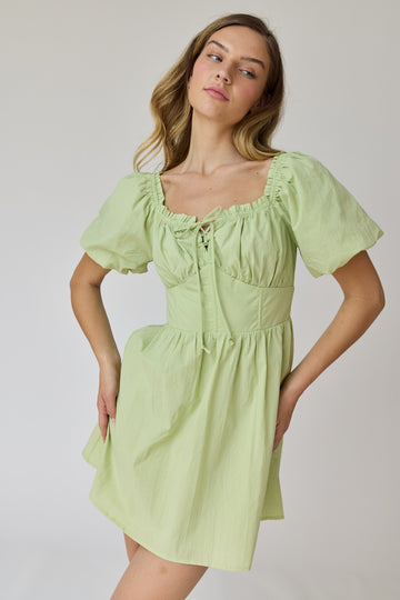 woman wearing a light green short puff sleeve dress with a lace-up detail and cinched waist