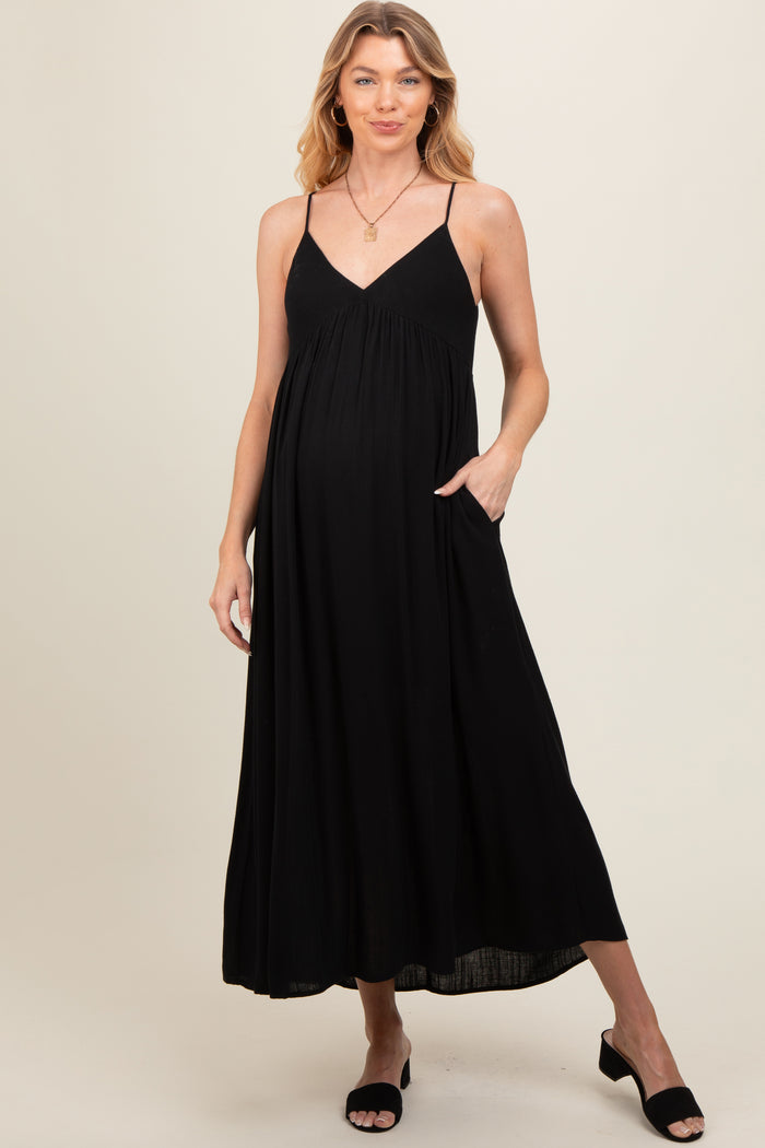 woman wearing a black maternity maxi dress with adjustable straps and pockets, showcasing her baby bump