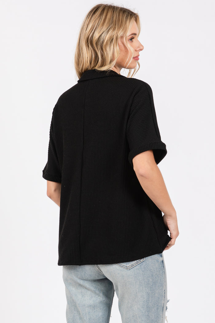 woman wearing a black short sleeve button-up shirt with rolled sleeves and a relaxed fit, seen from the back