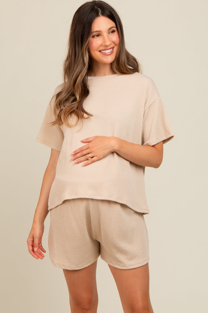 woman wearing a beige ribbed maternity top and matching shorts, holding her baby bump