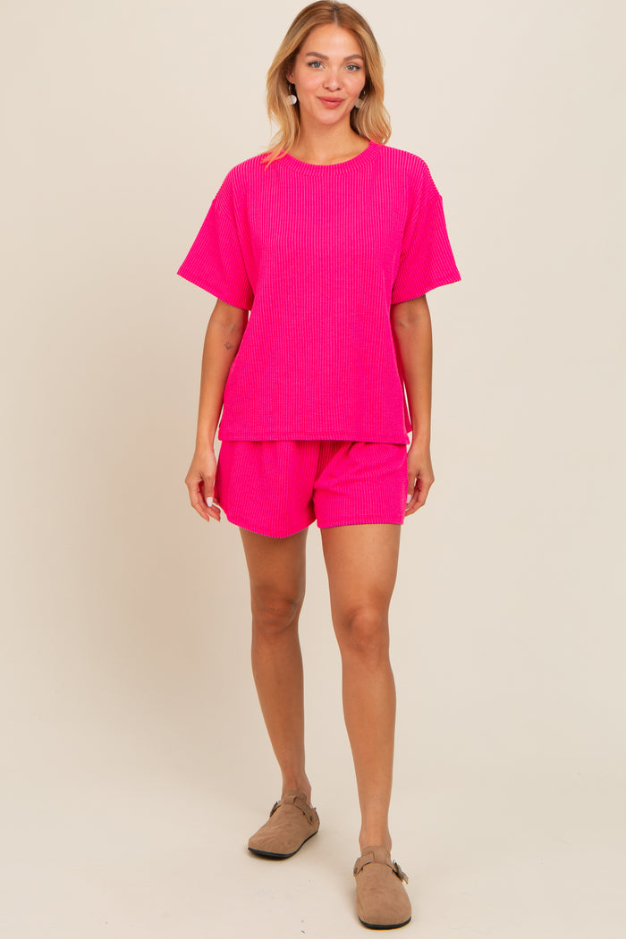 woman wearing a bright pink ribbed short-sleeve top and matching shorts, standing against a neutral background