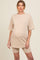 woman wearing a beige maternity oversized t-shirt dress with matching bike shorts, showing a visible baby bump