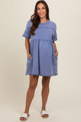 woman wearing a dusty blue short sleeve maternity dress with pockets and frayed hem, showing her baby bump