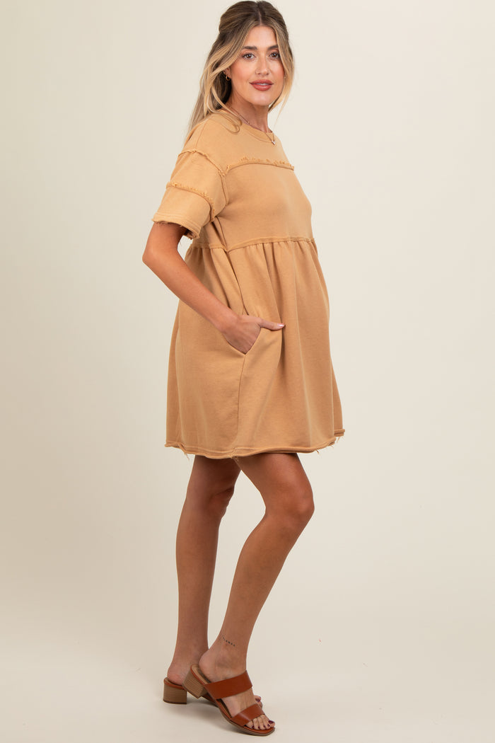 woman wearing a tan maternity dress with short sleeves and pockets, showing a baby bump