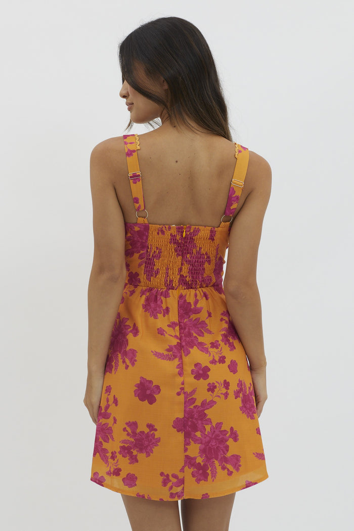 woman wearing a vibrant yellow floral sundress with pink patterns and a smocked back detail
