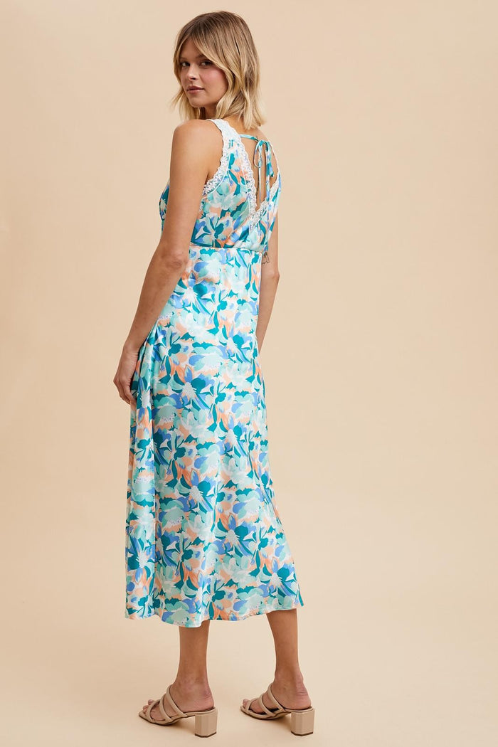 woman wearing a blue floral midi dress with a keyhole back and relaxed fit, standing against a beige background
