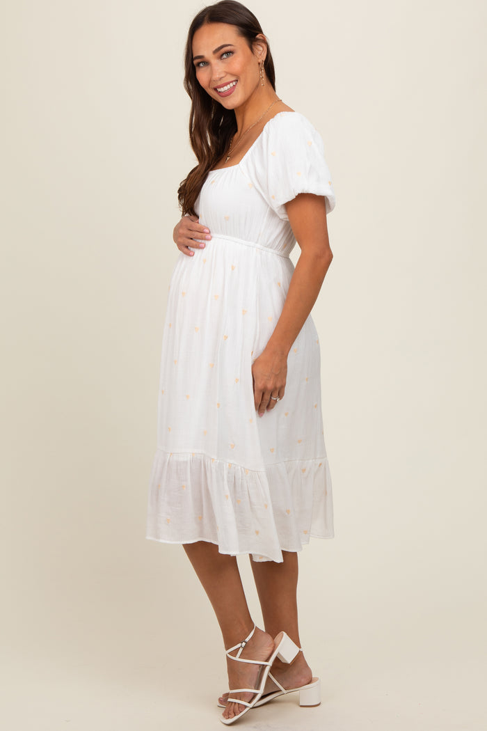 woman wearing a white maternity dress with floral details and puff sleeves, showing her baby bump