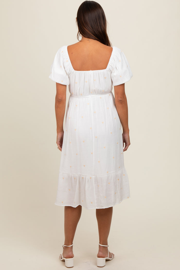 woman wearing a white maternity dress with puff sleeves and a tiered skirt, showing a slight baby bump from the back