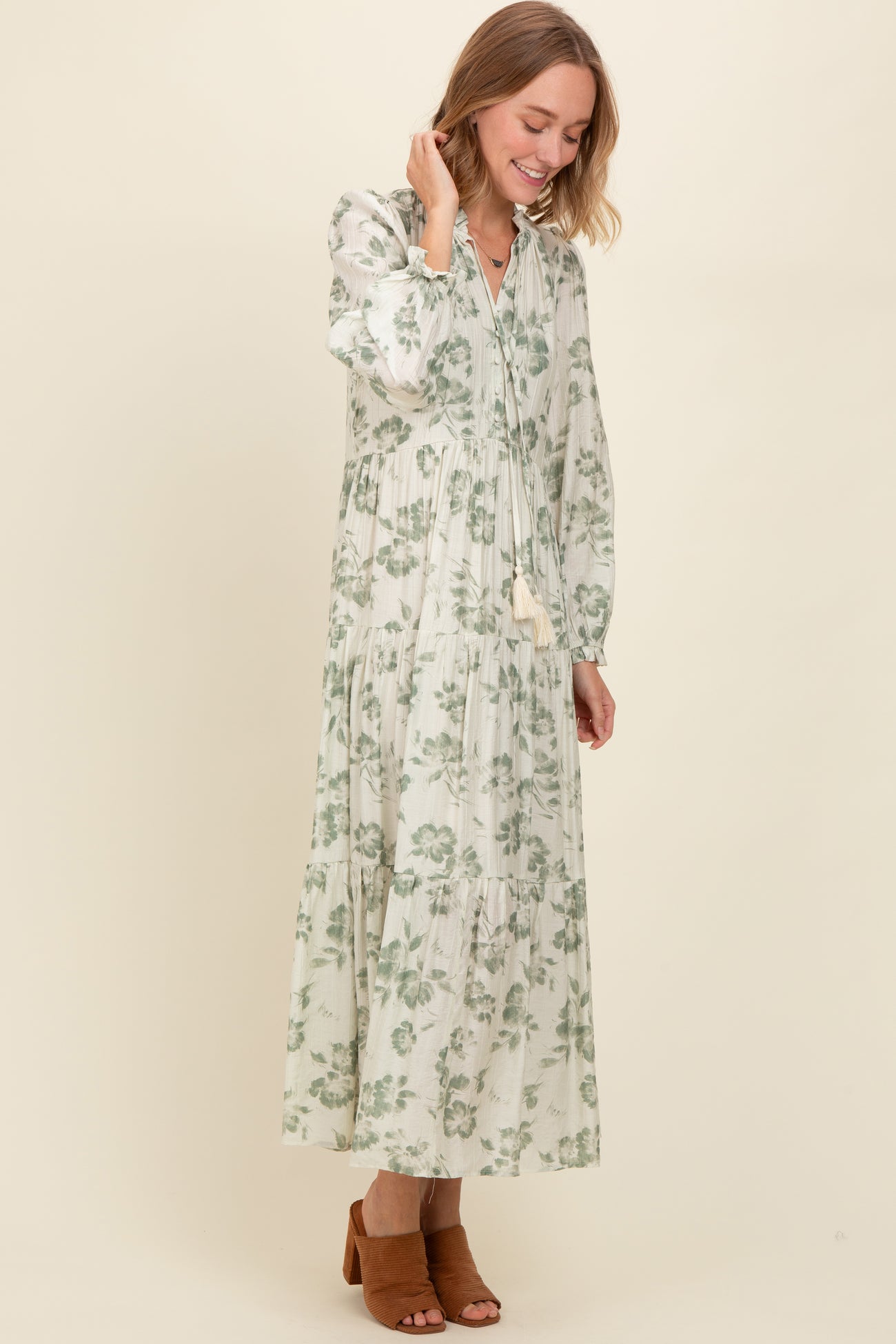 woman wearing a long sleeve green floral maxi dress with tiered detailing and a tassel tie neckline