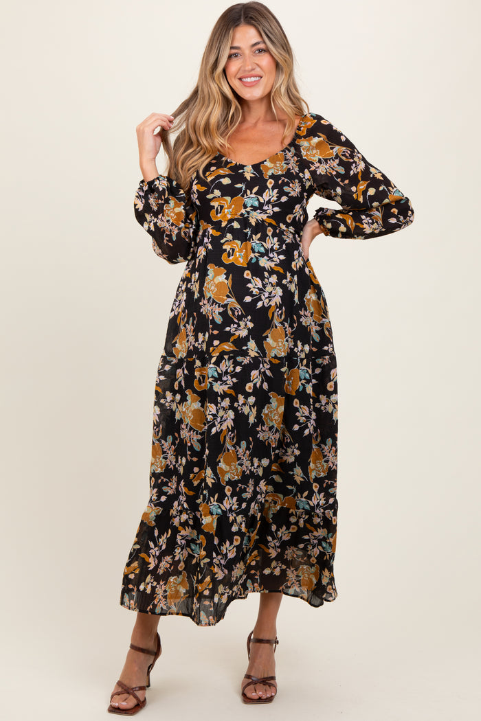 woman wearing a black floral maternity maxi dress with long sleeves and a fitted bodice, showing her baby bump