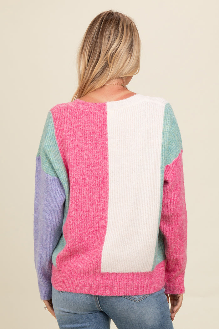 woman wearing a multicolored cozy sweater with pink, blue, and white panels, seen from the back