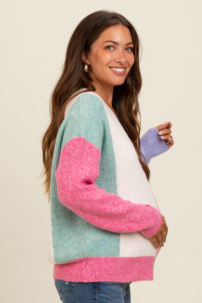 woman wearing a multi-colored striped maternity sweater, holding her baby bump, with shades of blue, pink, and purple