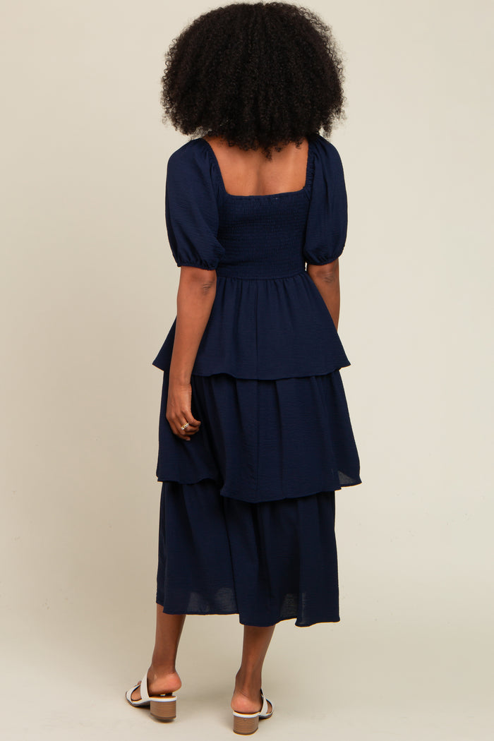woman wearing a navy blue tiered dress with puff sleeves, standing with her back to the camera