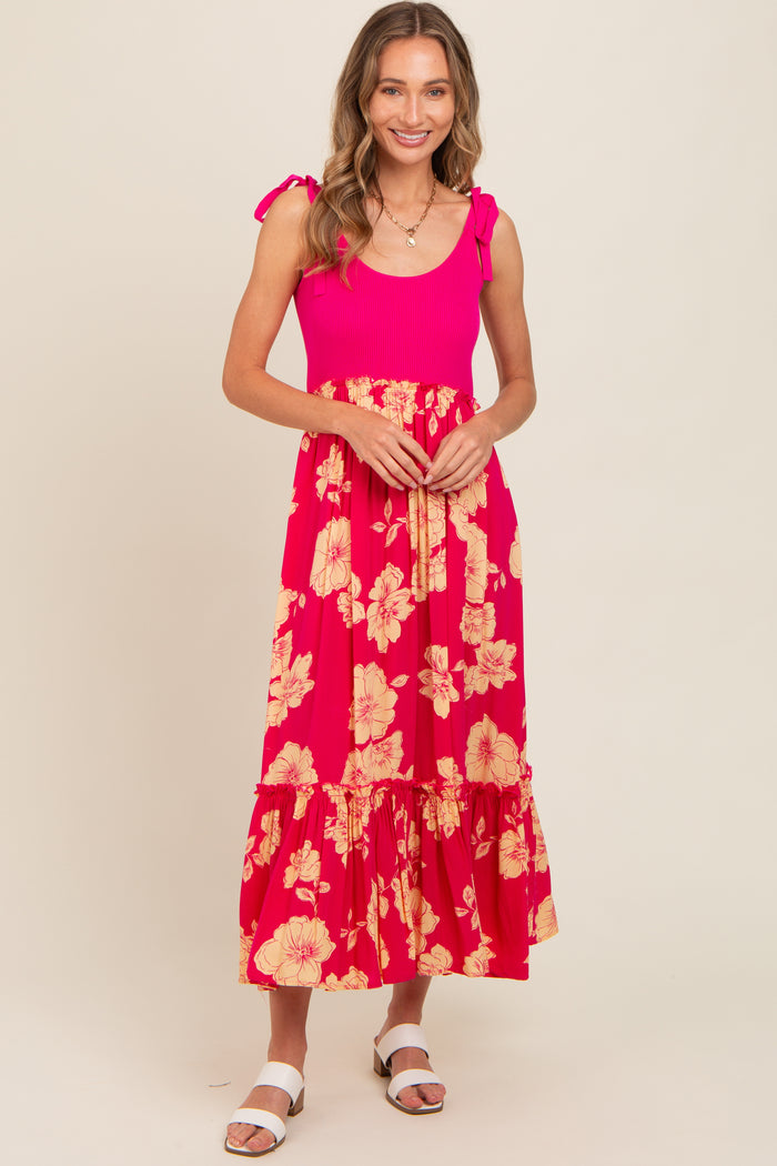 woman wearing a bright pink floral maxi dress with tie shoulder straps and a ruffled hem