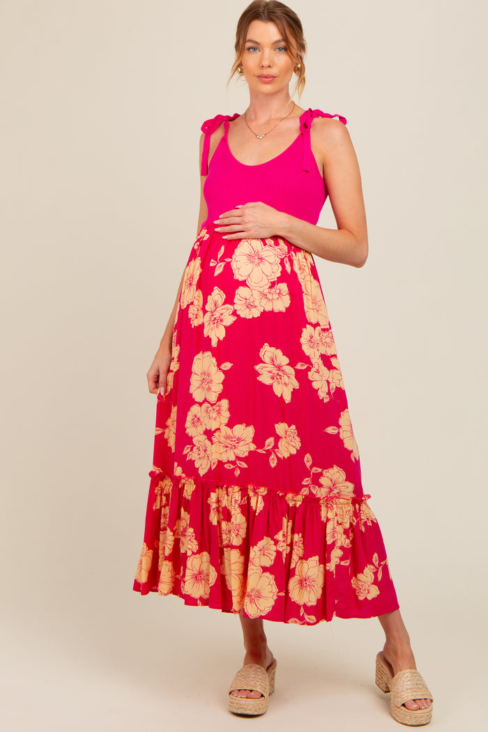 woman wearing a pink maternity maxi dress with floral print and ruffle hem, holding her baby bump