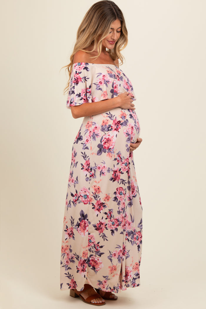woman wearing a floral off-the-shoulder maternity maxi dress and cradling her baby bump