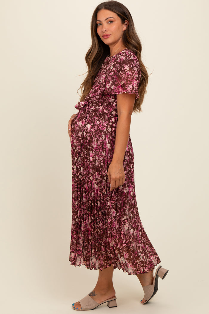 woman wearing a floral pleated maternity dress in shades of pink, holding her baby bump and smiling