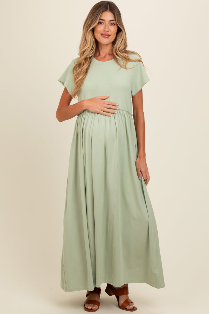 woman wearing a light green maxi maternity dress and holding her baby bump
