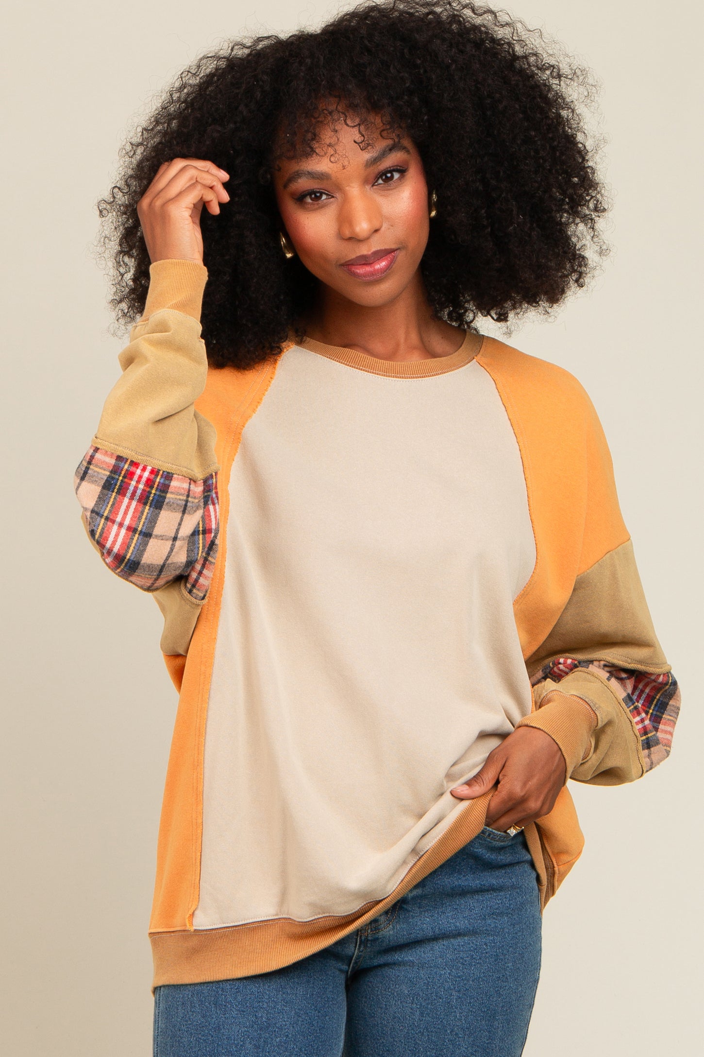 woman wearing a multicolored sweatshirt with plaid sleeves and a beige body, styled casually with denim jeans