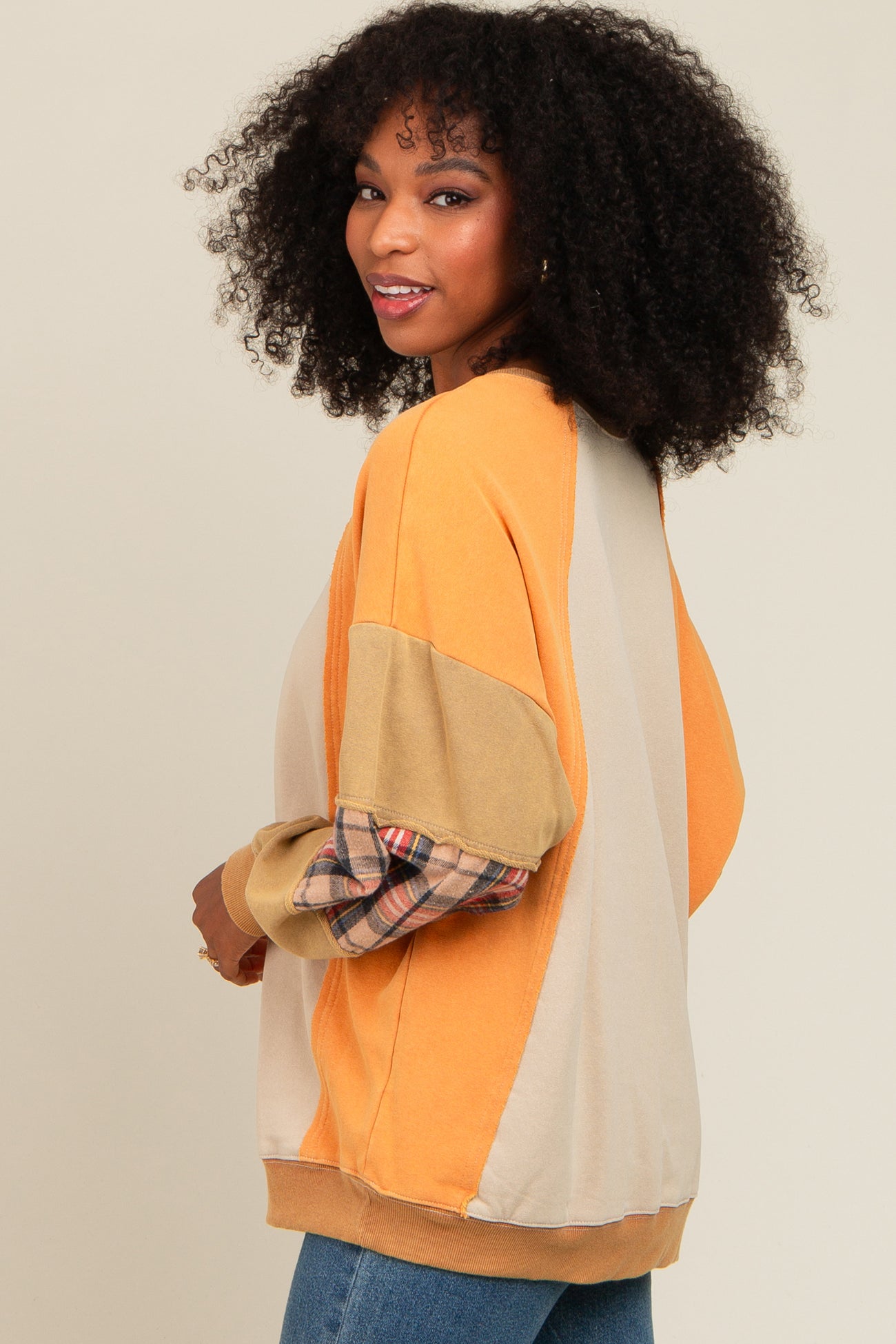 woman wearing an oversized color-blocked sweatshirt in orange and beige with plaid sleeve detail