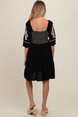 woman wearing a black maternity dress with embroidered sleeves and a fitted bodice, showing a relaxed, flowy skirt