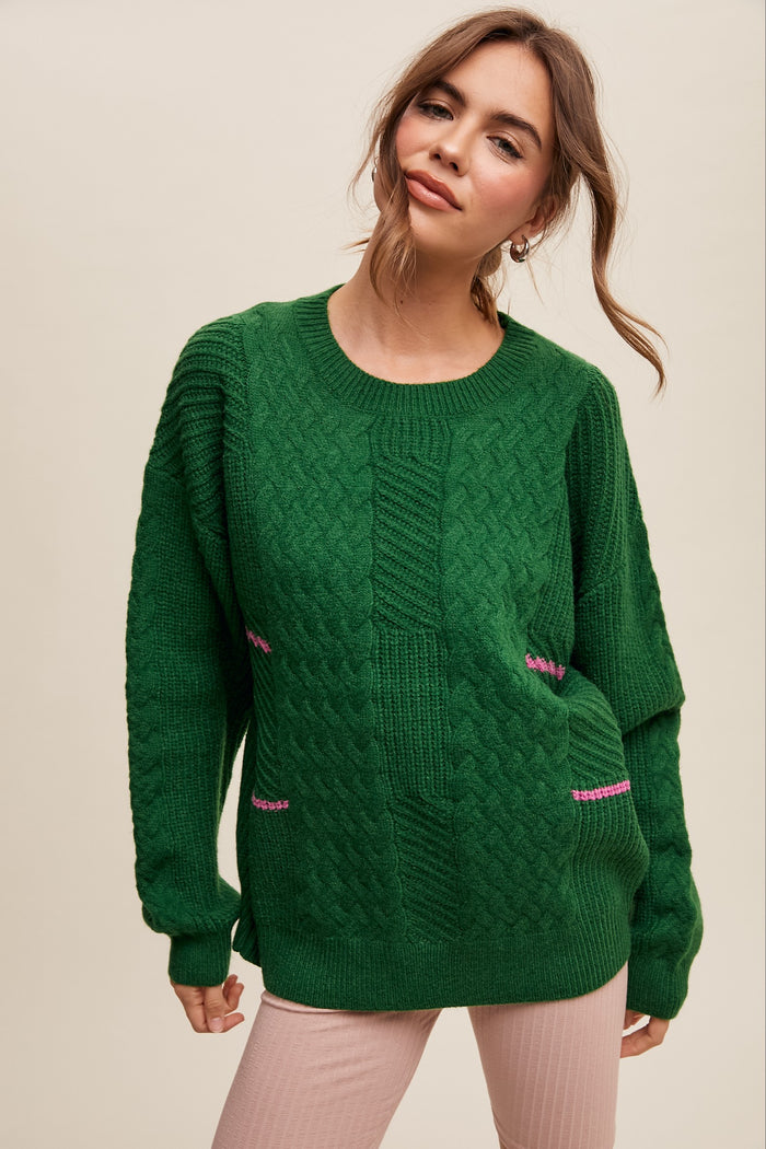 woman wearing a green cable knit sweater with contrasting pink detailing on the front