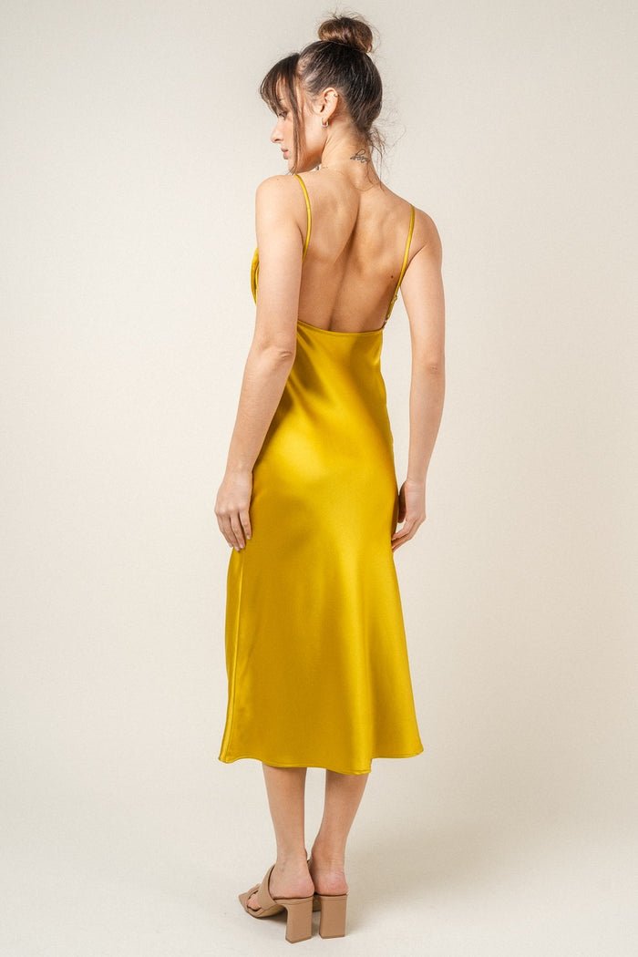 woman wearing a backless mustard yellow satin slip dress, showing a smooth silhouette and knee-length hem