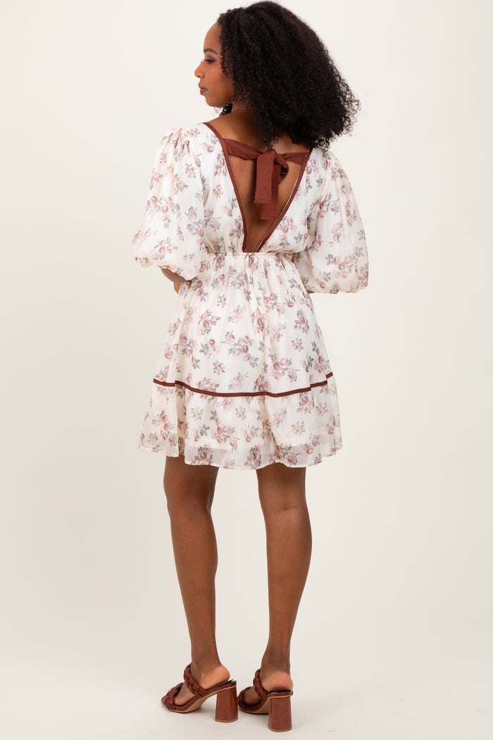 woman wearing a floral white short dress with puff sleeves and a back tie detail