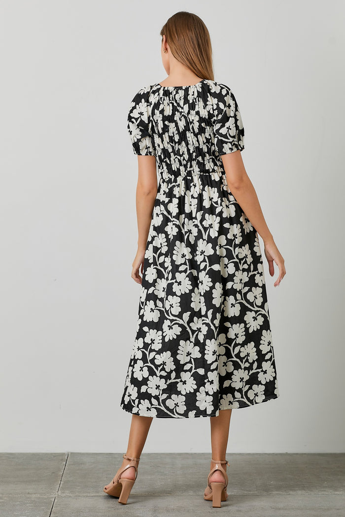 woman wearing a black and white floral midi dress with puff sleeves and a smocked waist seen from the back