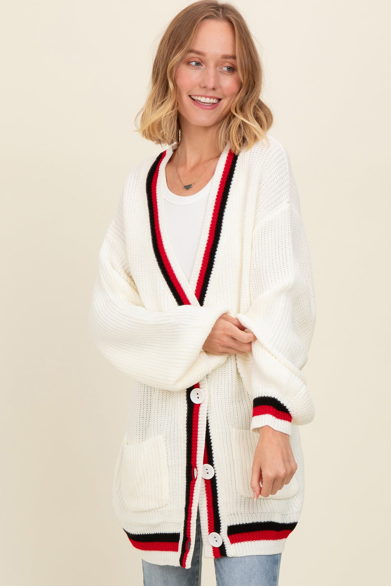 woman wearing an oversized white cardigan with red and black trim and pockets, styled with a casual look