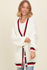 woman wearing an oversized white cardigan with red and black trim and pockets, styled with a casual look