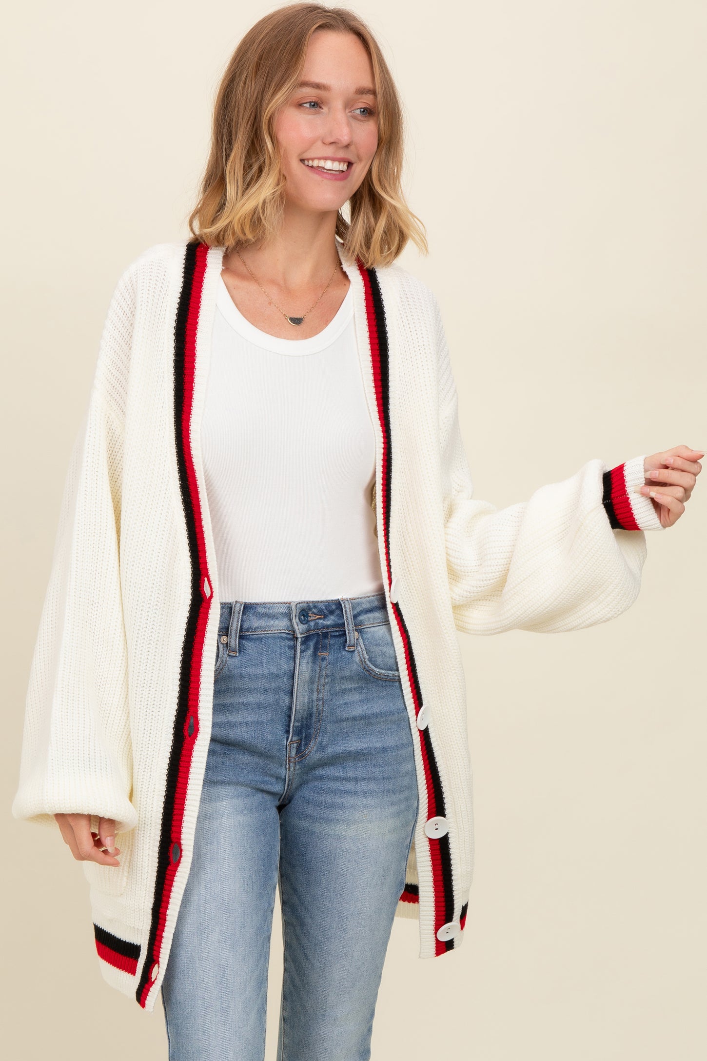 woman wearing a cream oversized cardigan with red and black detailing, paired with a white top and blue jeans
