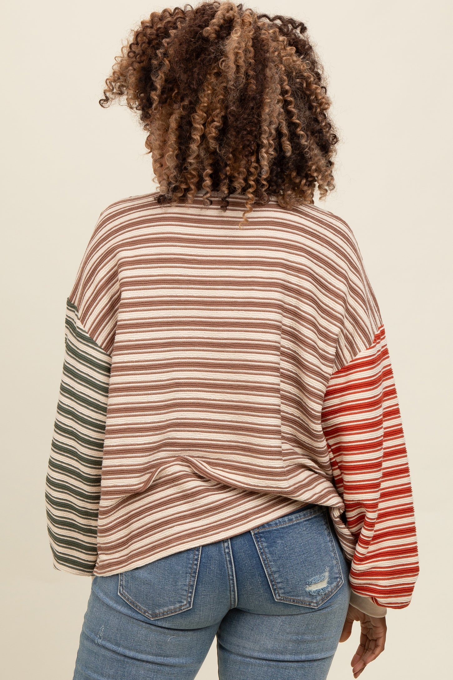 woman wearing a multicolor striped long sleeve top with green and red accents, paired with blue jeans