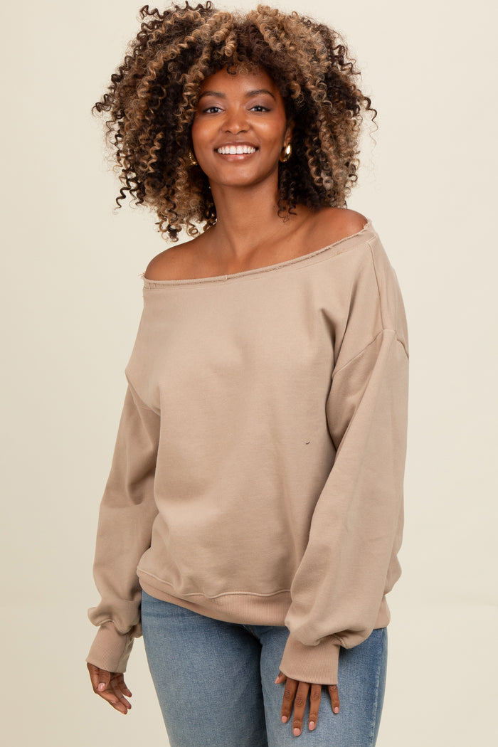 woman wearing a beige off-the-shoulder sweatshirt with long sleeves and relaxed fit, paired with blue jeans