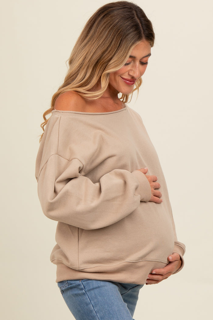 woman wearing a beige off-shoulder maternity sweater and holding her baby bump