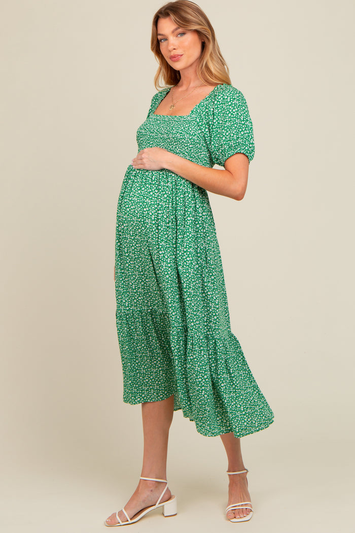 woman wearing a green floral maternity dress with short sleeves and a tiered skirt, holding her baby bump