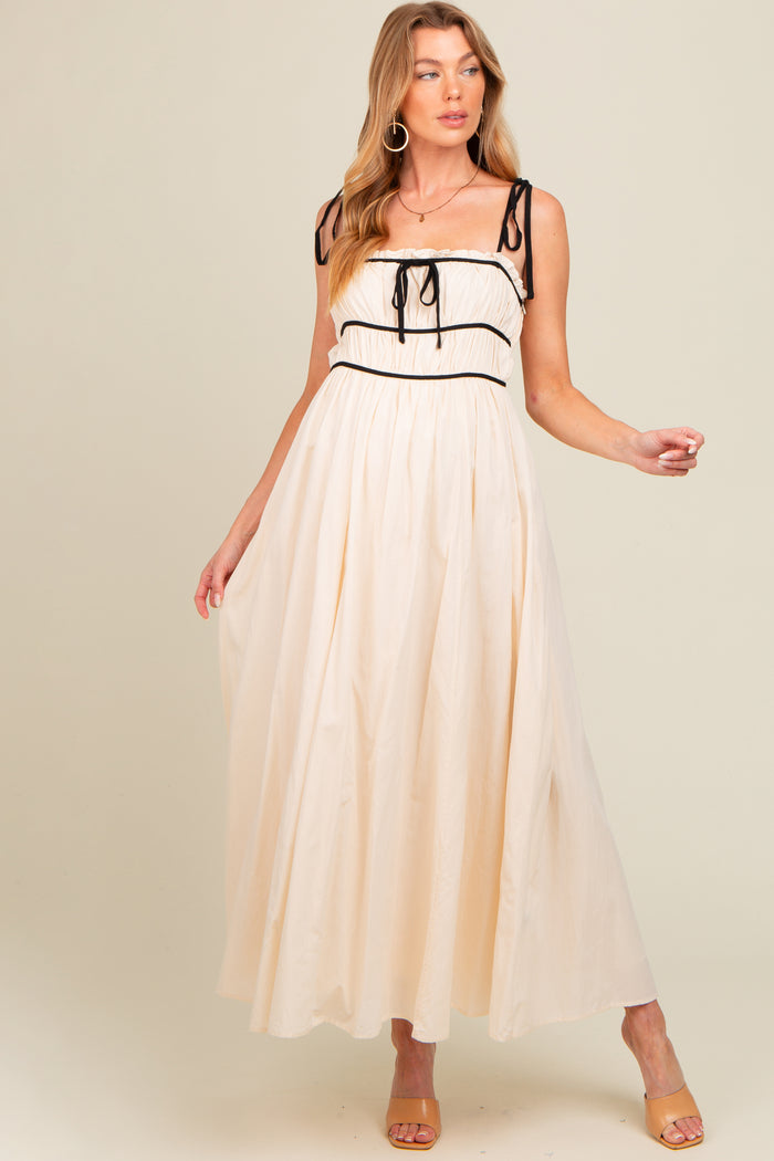 woman wearing a cream-colored maternity maxi dress with black piping and tie straps