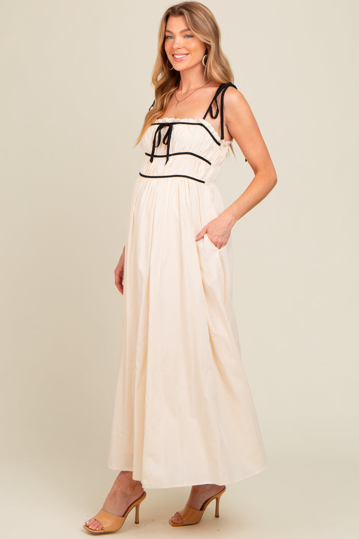 woman wearing a cream maternity maxi dress with black trim and pockets, smiling and standing sideways