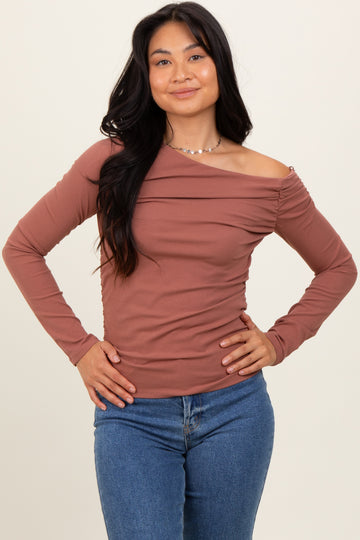 woman wearing a rust-colored off-the-shoulder long sleeve top with ruching detail and paired with blue jeans